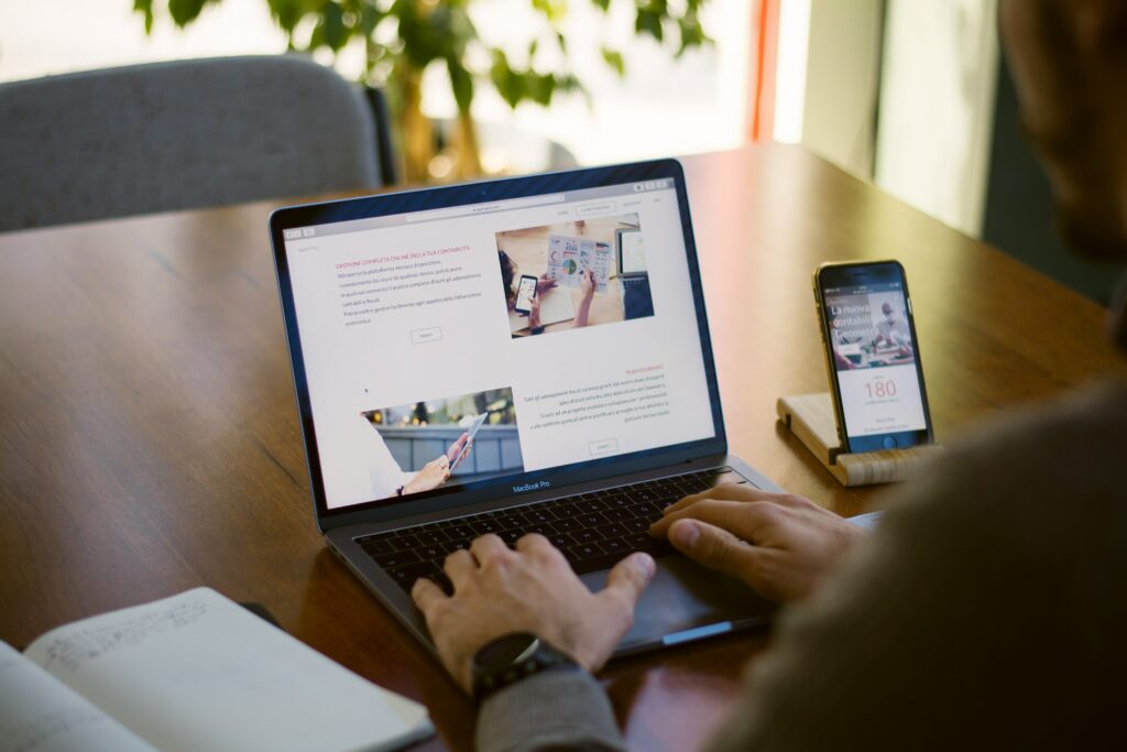 Persona al computer e con un cellulare mentre scrive un articolo su un sito web.